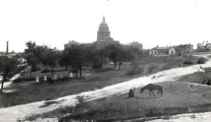 Photograph showing a horse grazing and young women walking across the grassy space northeast of the Capitol building