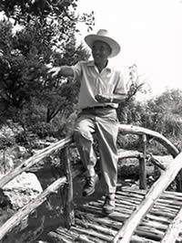 Photograph of Isamu Taniguchi sitting on bridge over pond in Oriental Garden