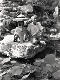 Photograph of Taniguchi kneeling on rock beside pagoda sculpture in Oriental Garden