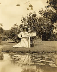 Photo of woman beside lake with sign saying do not pick the flowers