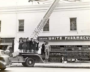 Photograph of Mayor Tom Miller on fire truck in front of White Pharmacy sign