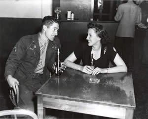 Photograph of young man in uniform with a young woman in conversation over soft drinks