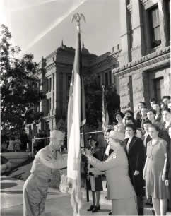 Photograph of uniformed man and woman holding flagpole with other women in background