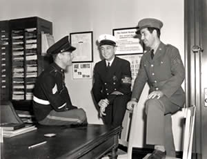 Photograph of three uniformed service men in recruiting office