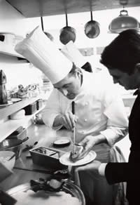 Photograph of chef serving food onto a plate for a waiter