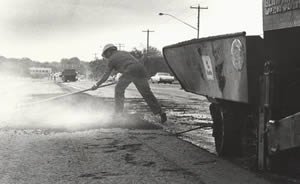 Photograph of man in hard hat spreading asphalt