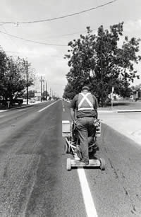 Photograph of man riding a machine that paints stripes in the street
